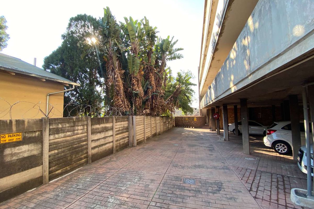 Exterior view of the apartment complex parking area featuring paved driveway, covered parking bays, and perimeter boundary wall with security fencing.