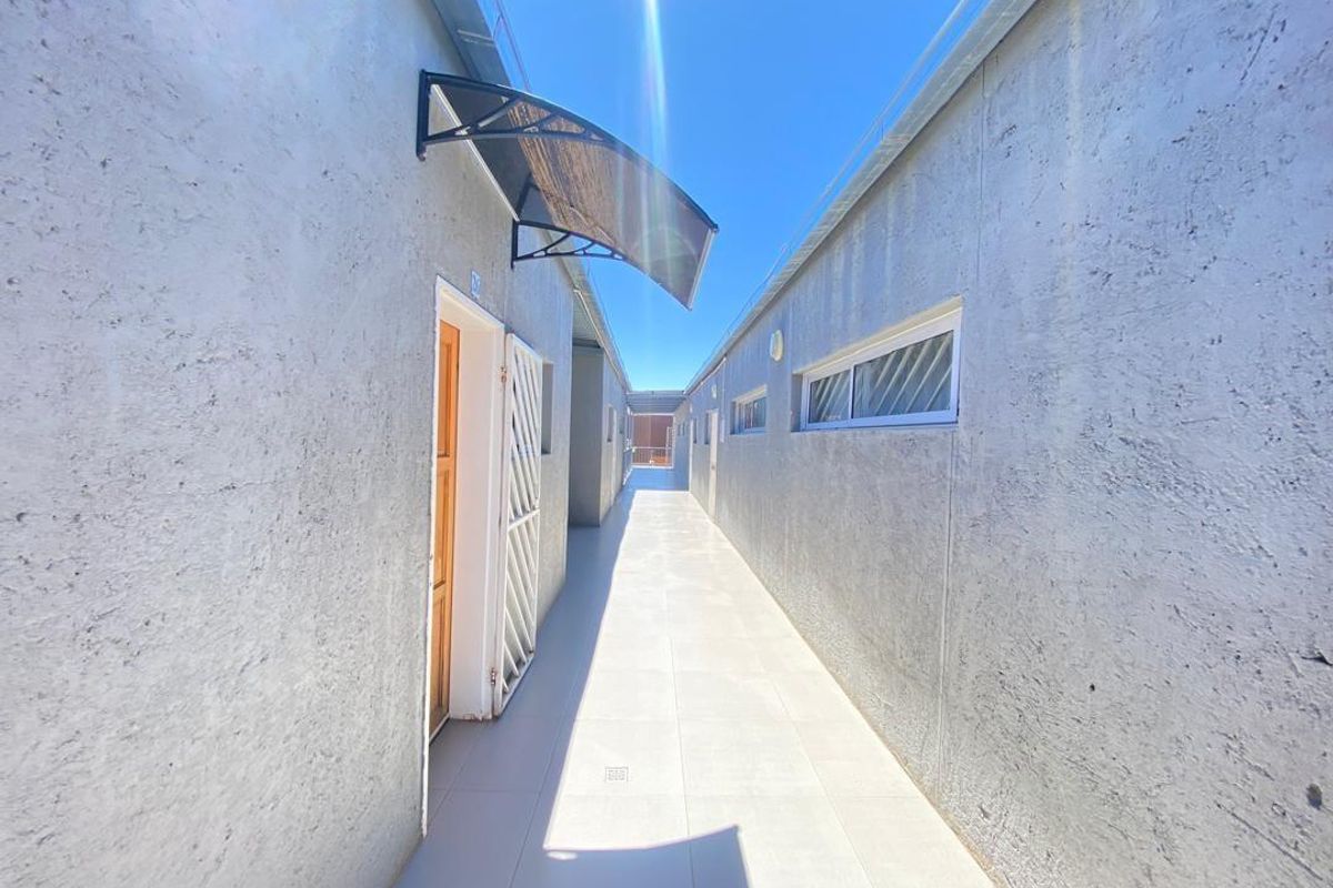 An exterior walkway or corridor featuring tiled flooring, textured wall finishes, and protective door awnings, providing access to multiple apartment units.