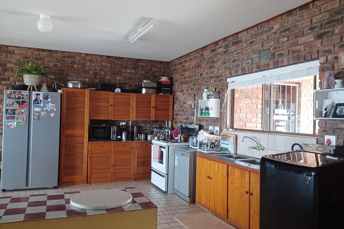 A functional kitchen featuring exposed brick walls, wooden cabinetry, tiled flooring, and a double sink with a window view.