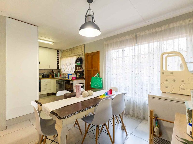 Open-plan dining area adjacent to a functional kitchen with built-in cabinetry, tiled flooring, and natural light through large windows.