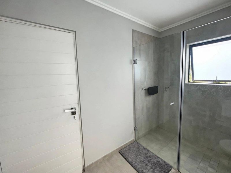 A modern bathroom featuring a frameless glass shower enclosure with neutral wall and floor tiling and a top-hung window for natural light.