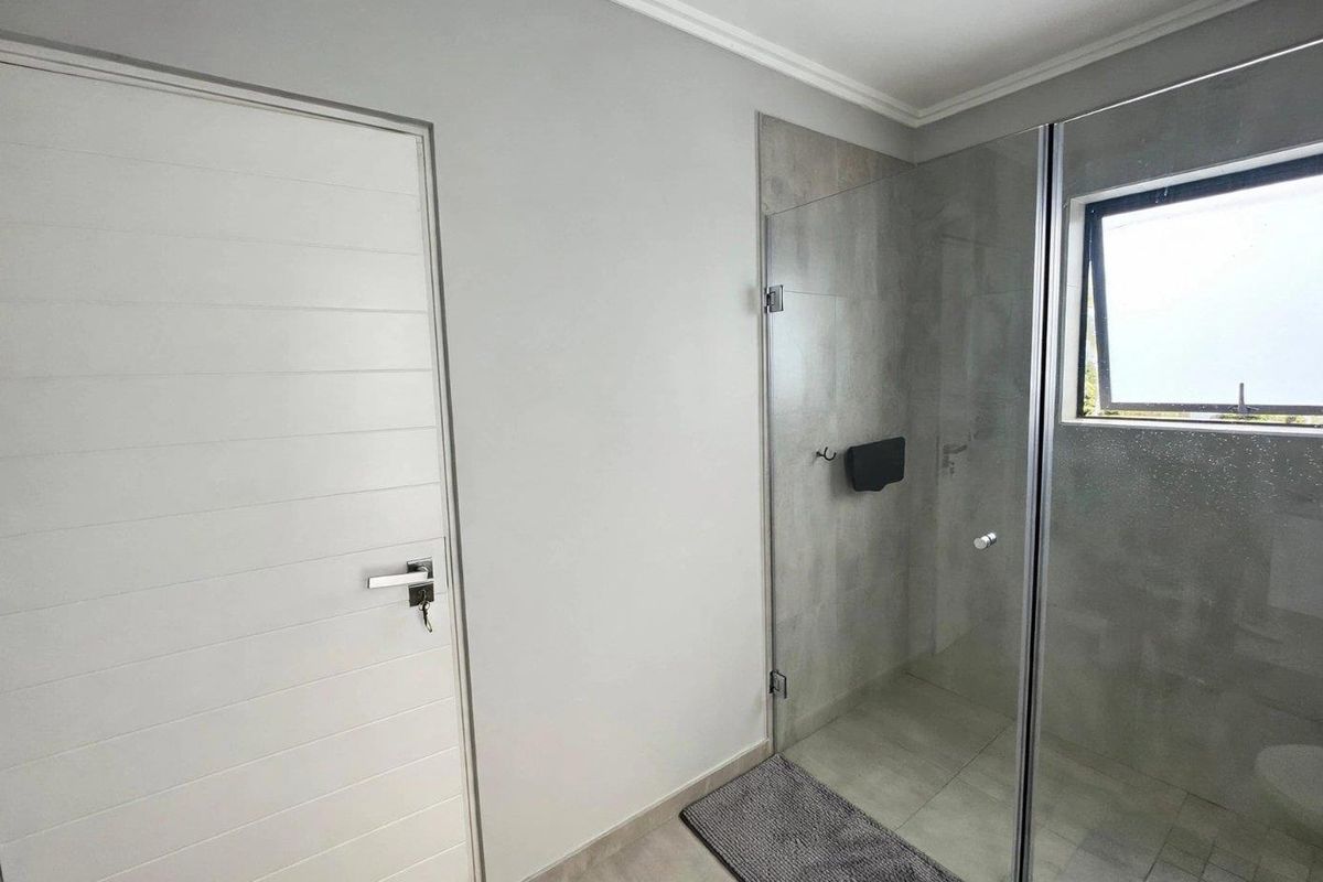 A modern bathroom featuring a frameless glass shower enclosure with neutral wall and floor tiling and a top-hung window for natural light.