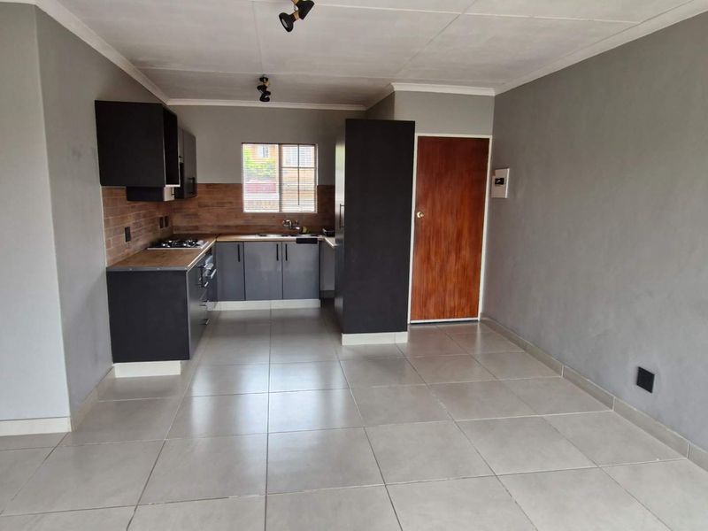 An open-plan living and kitchen area featuring modern dark cabinetry, tiled flooring, and a neutral grey wall finish.