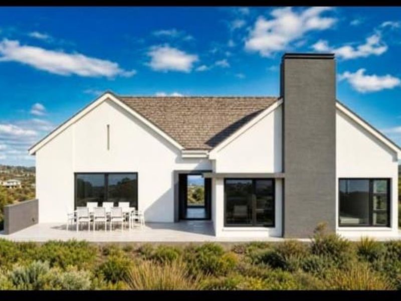 Modern rear elevation featuring a covered patio, large windows, and a prominent chimney, set against a landscaped garden with scenic views.