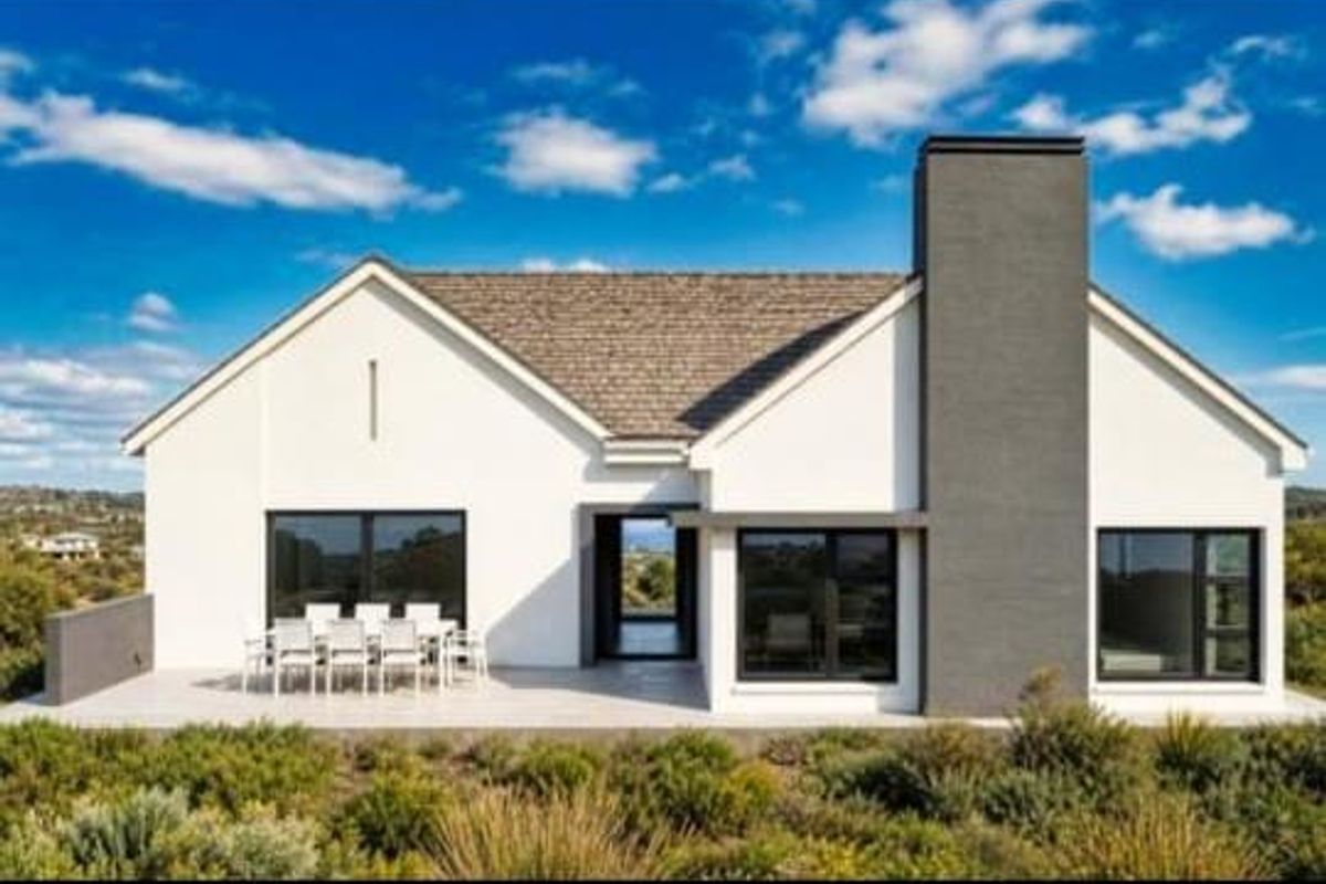 Modern rear elevation featuring a covered patio, large windows, and a prominent chimney, set against a landscaped garden with scenic views.