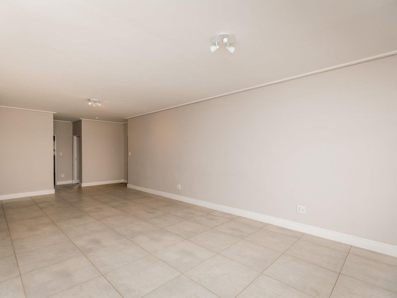 A spacious, empty living area featuring neutral wall tones, tiled flooring, and modern ceiling-mounted spotlights, providing a clean canvas for interior design.