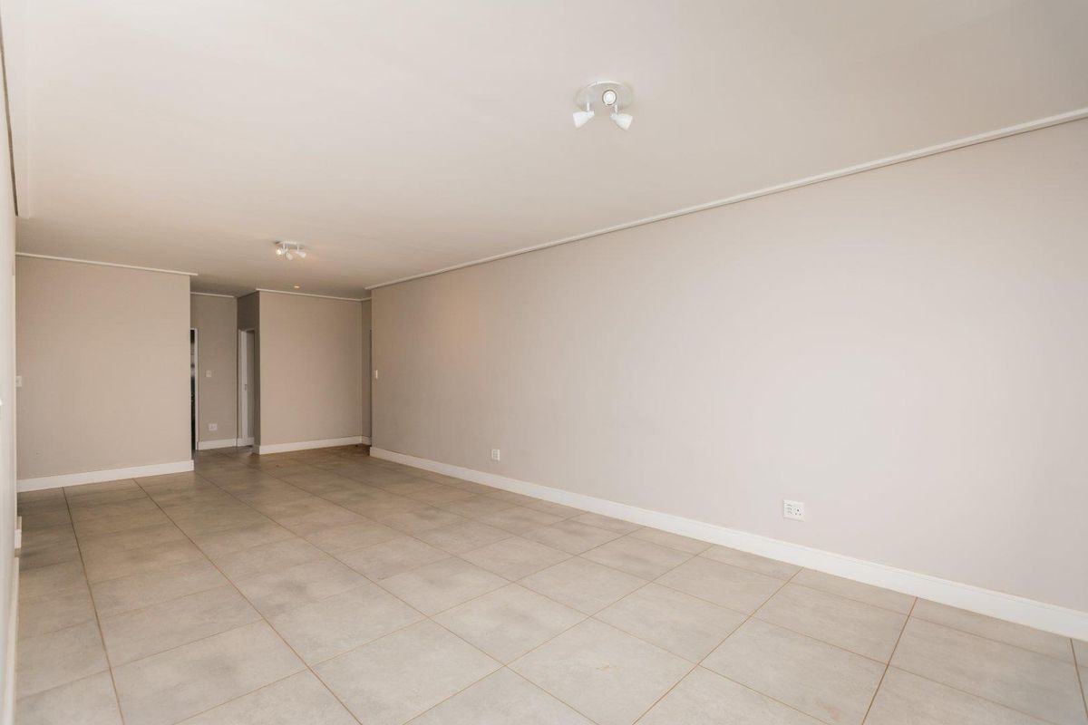 A spacious, empty living area featuring neutral wall tones, tiled flooring, and modern ceiling-mounted spotlights, providing a clean canvas for interior design.