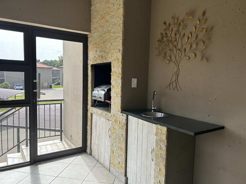 Covered balcony featuring a built-in braai, stone-clad finish, granite countertop with sink, and tiled flooring, offering a functional outdoor entertainment space.