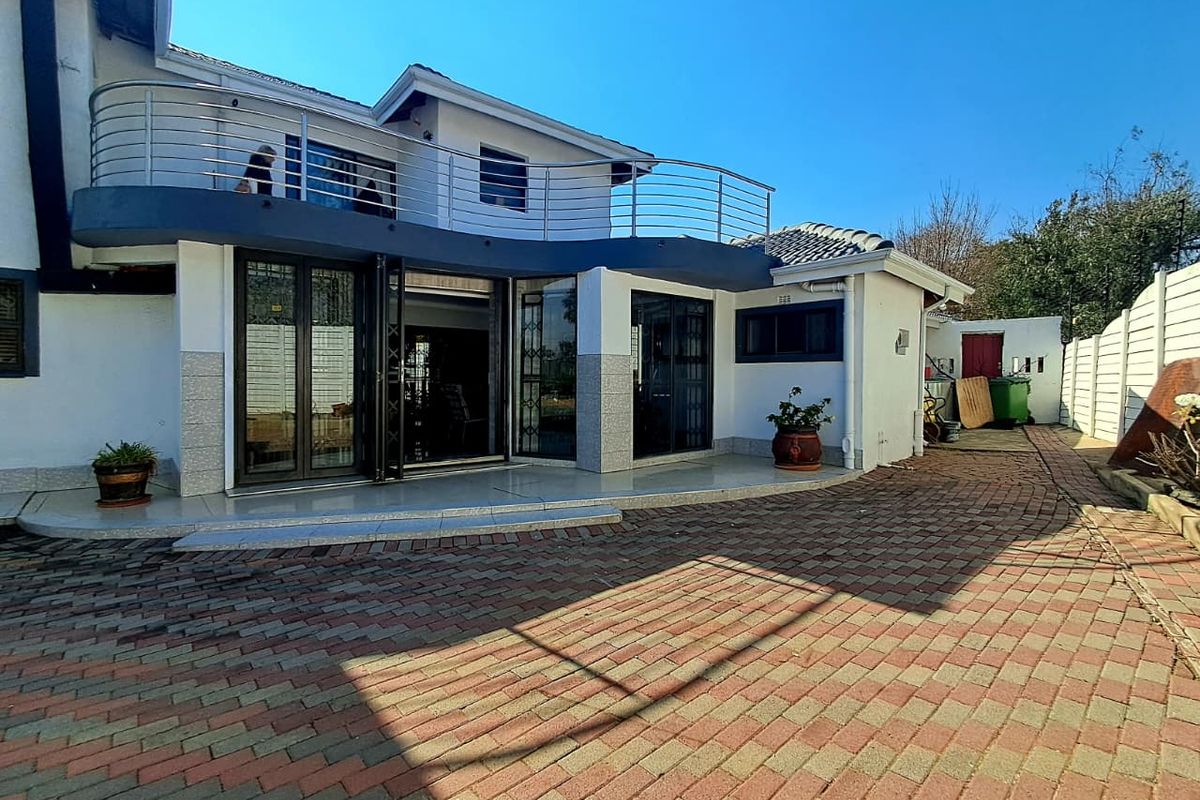 Rear view of the property featuring a paved courtyard, a tiled patio area, and an upper-level balcony with stainless steel railings.