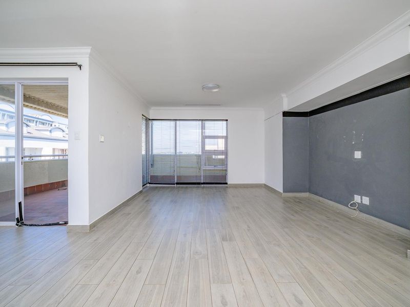 A bright, empty living room featuring light-toned laminate flooring, modern grey accent wall, and sliding glass doors leading to an outdoor balcony.