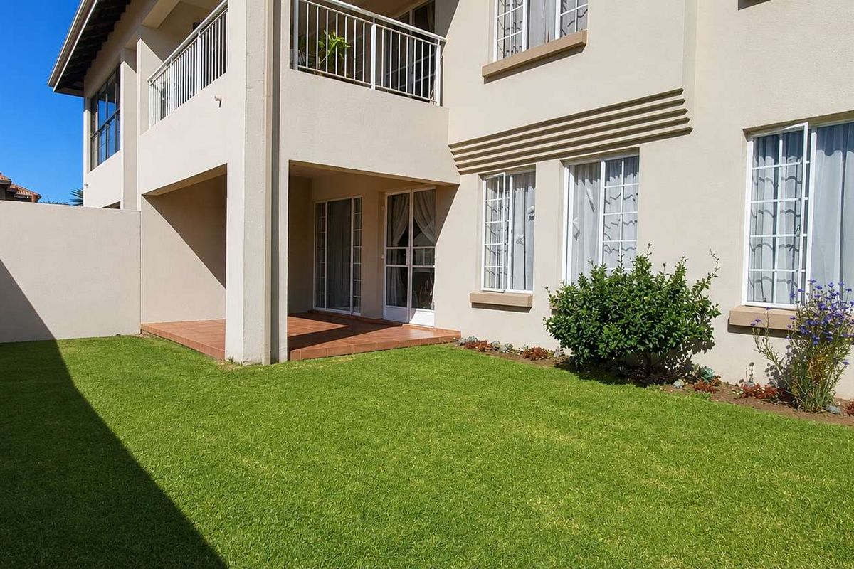 A well-maintained rear garden featuring a manicured lawn, a covered patio area, and a balcony above, providing a private outdoor space.