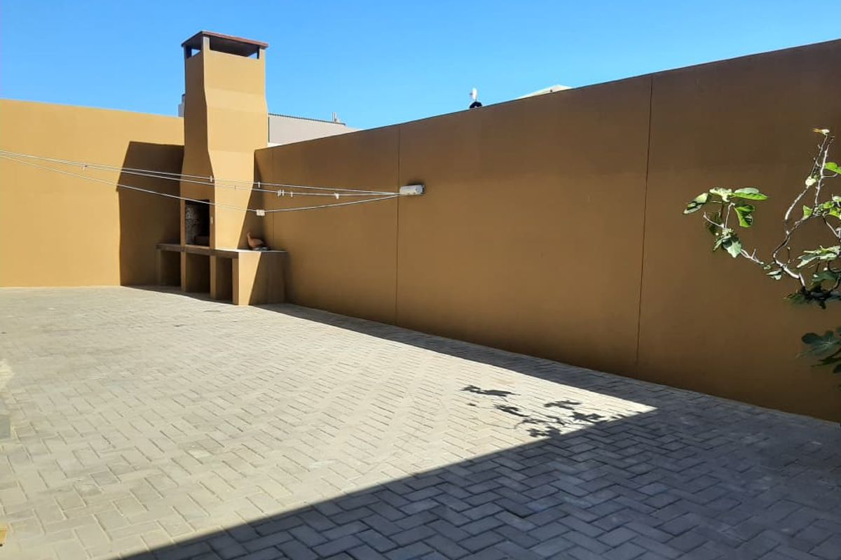 A paved outdoor courtyard featuring a built-in masonry braai or fireplace against a high boundary wall.
