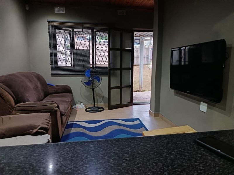 A living room featuring tiled flooring, a timber ceiling, and direct access to the exterior through a security-fitted door.