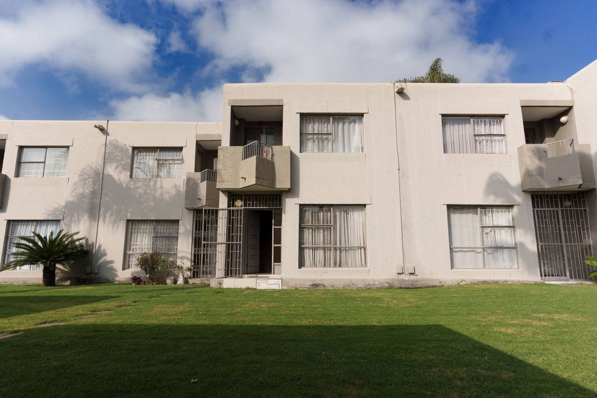 Rear view of a multi-story townhouse complex featuring a shared lawn, concrete facade, and security gates on ground floor entrances.