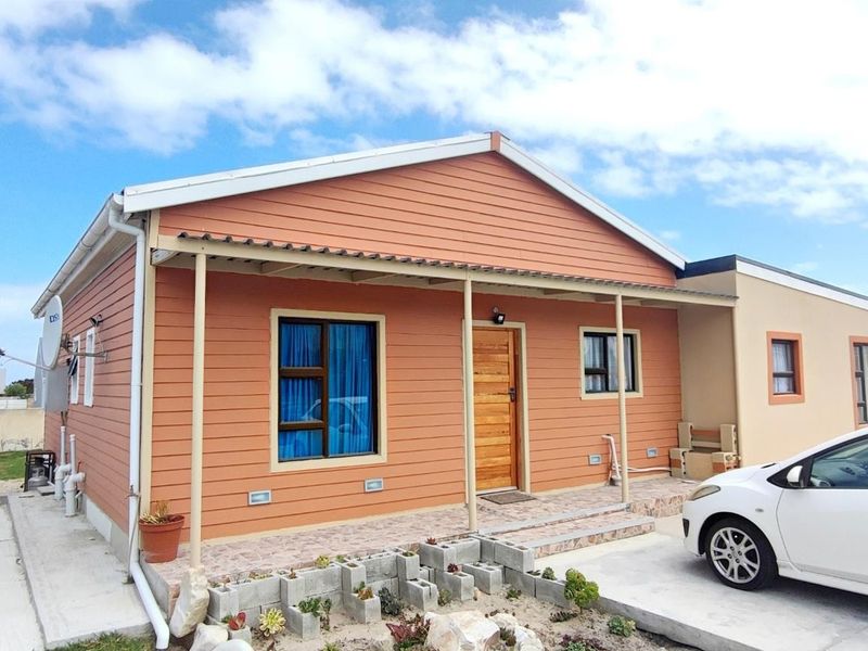 Front view of a single-story house featuring timber-look cladding, a covered patio area, and a concrete driveway with boundary walling.