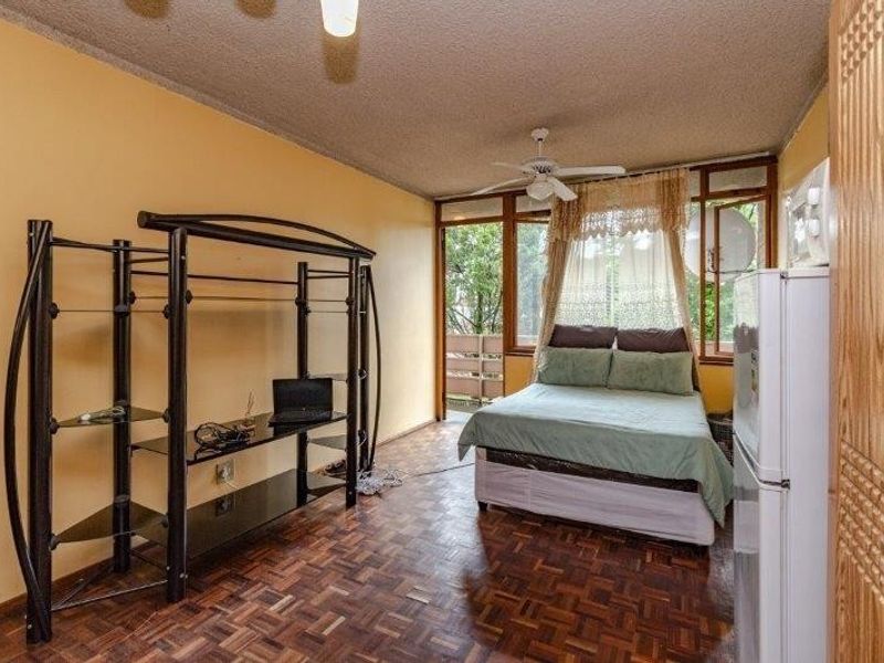 A bedroom featuring parquet flooring, a ceiling fan, and direct access to a balcony through large windows.