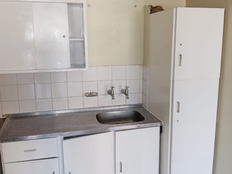 A dated kitchen area featuring a stainless steel sink, tiled splashback, and built-in white cabinetry requiring maintenance and cosmetic updates.