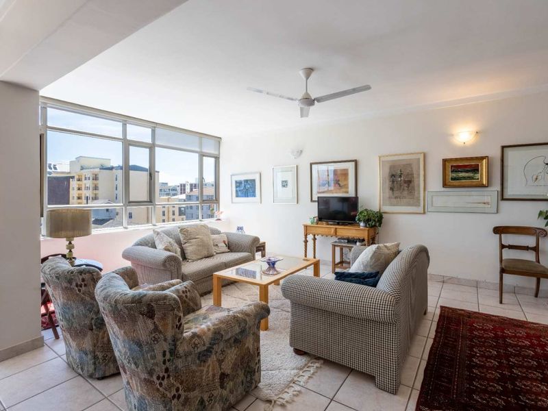 A bright and spacious living room featuring large aluminium-framed windows, tiled flooring, and a ceiling fan, offering a comfortable and well-lit living area.