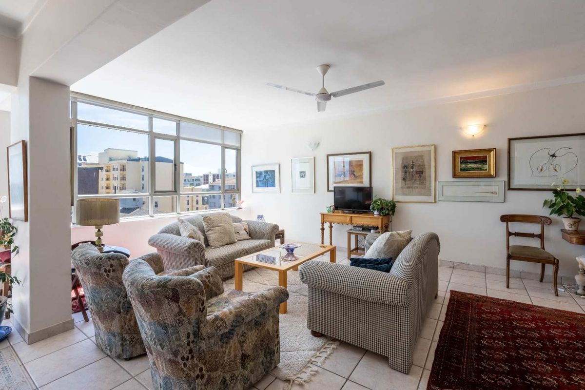 A bright and spacious living room featuring large aluminium-framed windows, tiled flooring, and a ceiling fan, offering a comfortable and well-lit living area.