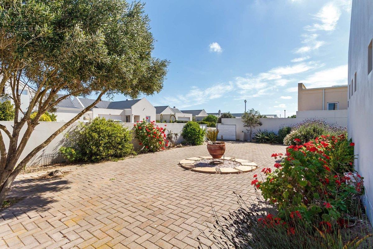 A well-maintained paved rear courtyard area featuring established garden beds, mature trees, and secure boundary walls.