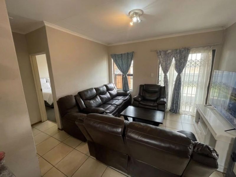A comfortable living room featuring tiled flooring, a sliding door with security gate, and neutral wall finishes, providing a functional and well-lit space.