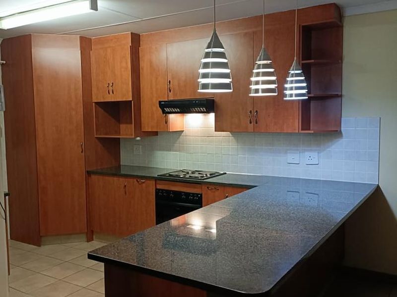 A functional kitchen featuring wooden cabinetry, granite countertops, a gas hob, built-in oven, and tiled backsplash with modern pendant lighting.