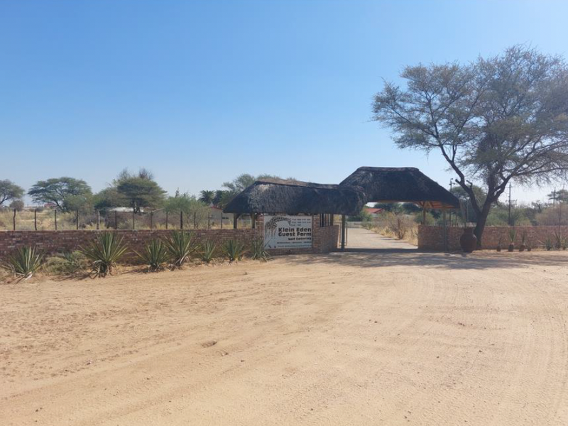 Entrance view of the small holding featuring a thatched gate structure, brick boundary wall, and a gravel driveway leading into the property.