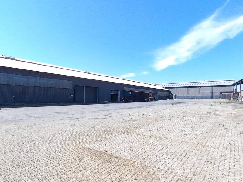 Expansive industrial yard featuring paved surfacing, large warehouse structures with corrugated metal cladding, and a covered steel canopy area.