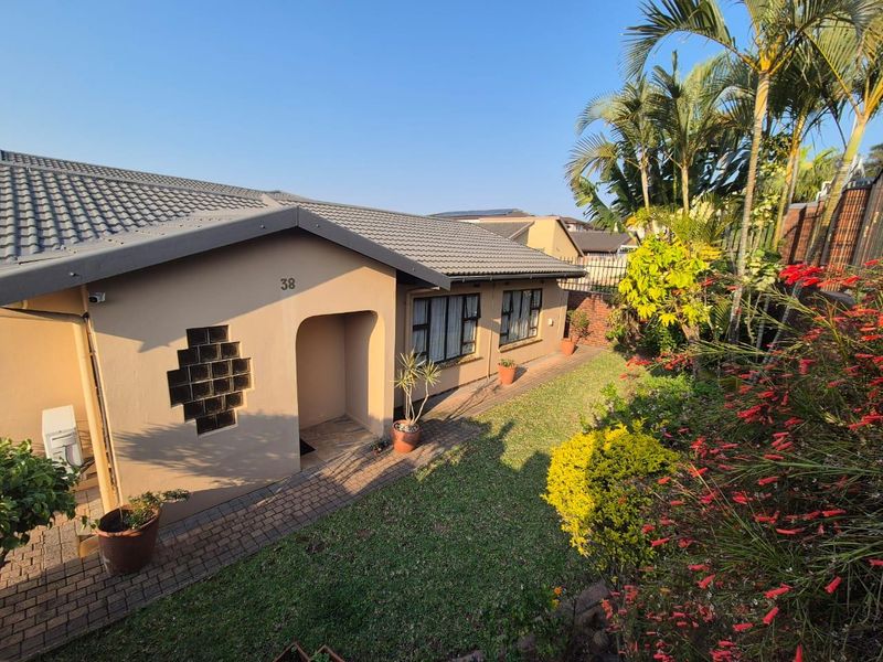 A well-maintained front exterior view of the house featuring a tiled roof, paved walkway, and established garden landscaping.