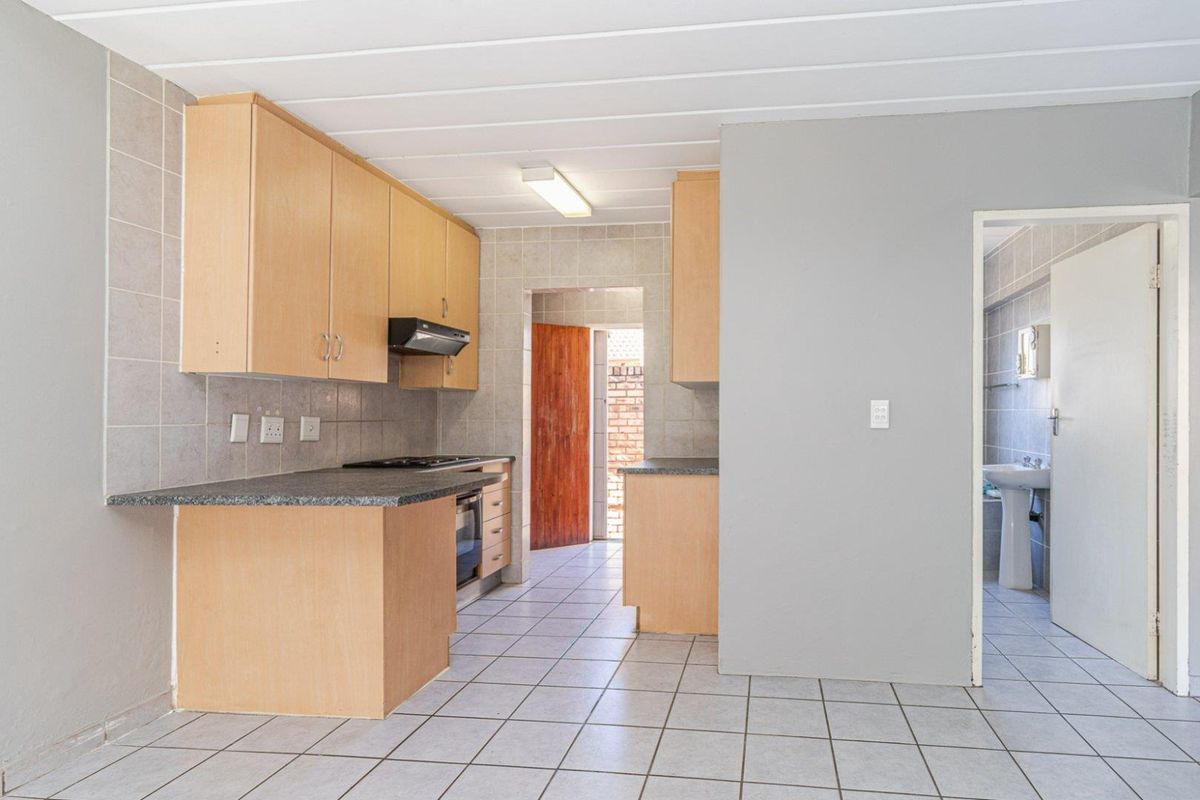 A functional kitchen featuring light wood cabinetry, dark laminate countertops, tiled flooring, and an integrated oven and extractor fan.