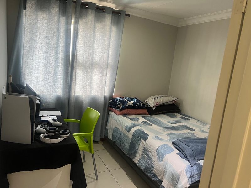 A compact bedroom featuring tiled flooring and neutral wall finishes, suitable for a single bed and workspace setup.