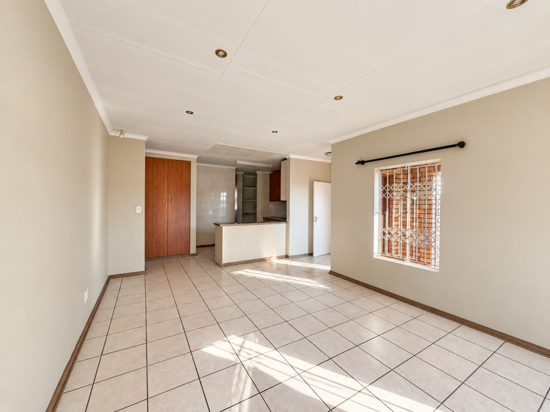 An open-plan living and kitchen area featuring neutral tiled flooring, recessed lighting, and built-in cabinetry, offering a clean and versatile space.