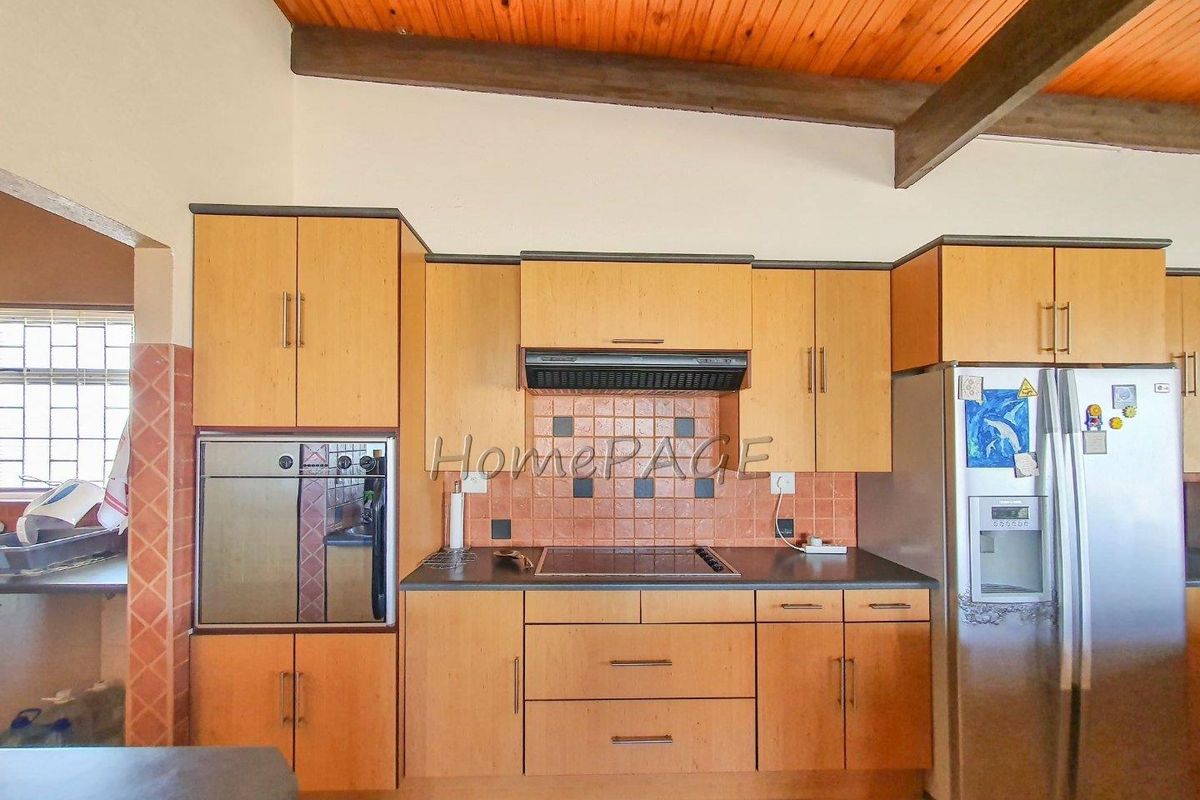 A functional kitchen featuring wood-finish cabinetry, a built-in oven, electric hob with extractor fan, and a tiled backsplash under a vaulted timber ceiling.