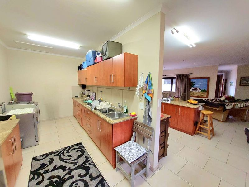 A functional scullery area featuring built-in wooden cabinetry, granite countertops, and a double stainless steel sink, adjacent to the main living space.