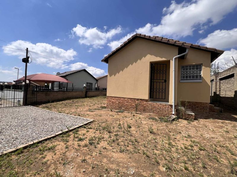 Rear view of a detached house featuring a tiled roof, brick plinth, and secure metal gates, set within an unlandscaped yard with perimeter walling.