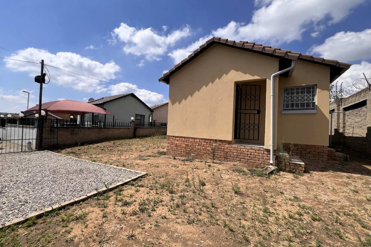 Rear view of a detached house featuring a tiled roof, brick plinth, and secure metal gates, set within an unlandscaped yard with perimeter walling.