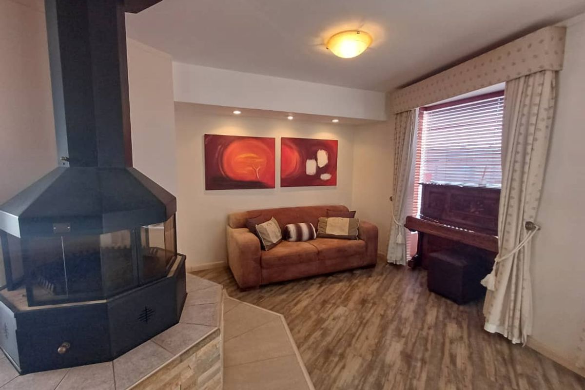 A cozy living room featuring a prominent central freestanding fireplace with a tiled hearth and wood-look flooring.
