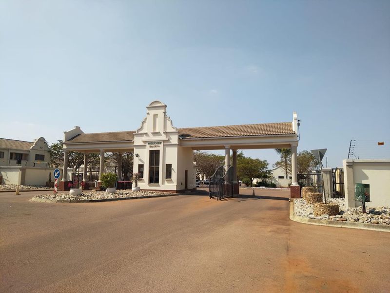 The main entrance gate of the residential complex featuring a secure guard house, paved driveway, and well-maintained architectural facade.
