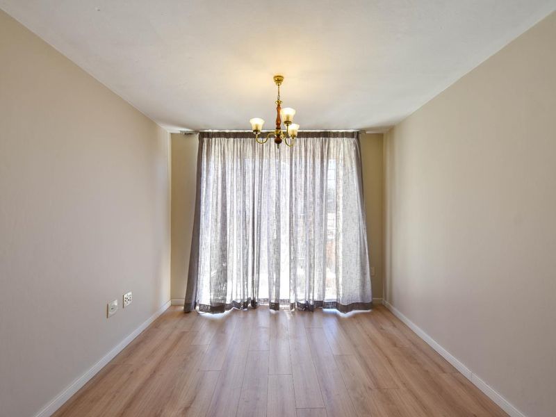 A bright and empty living room featuring light wood-look laminate flooring, neutral walls, and a sliding glass door with curtains leading to the exterior.