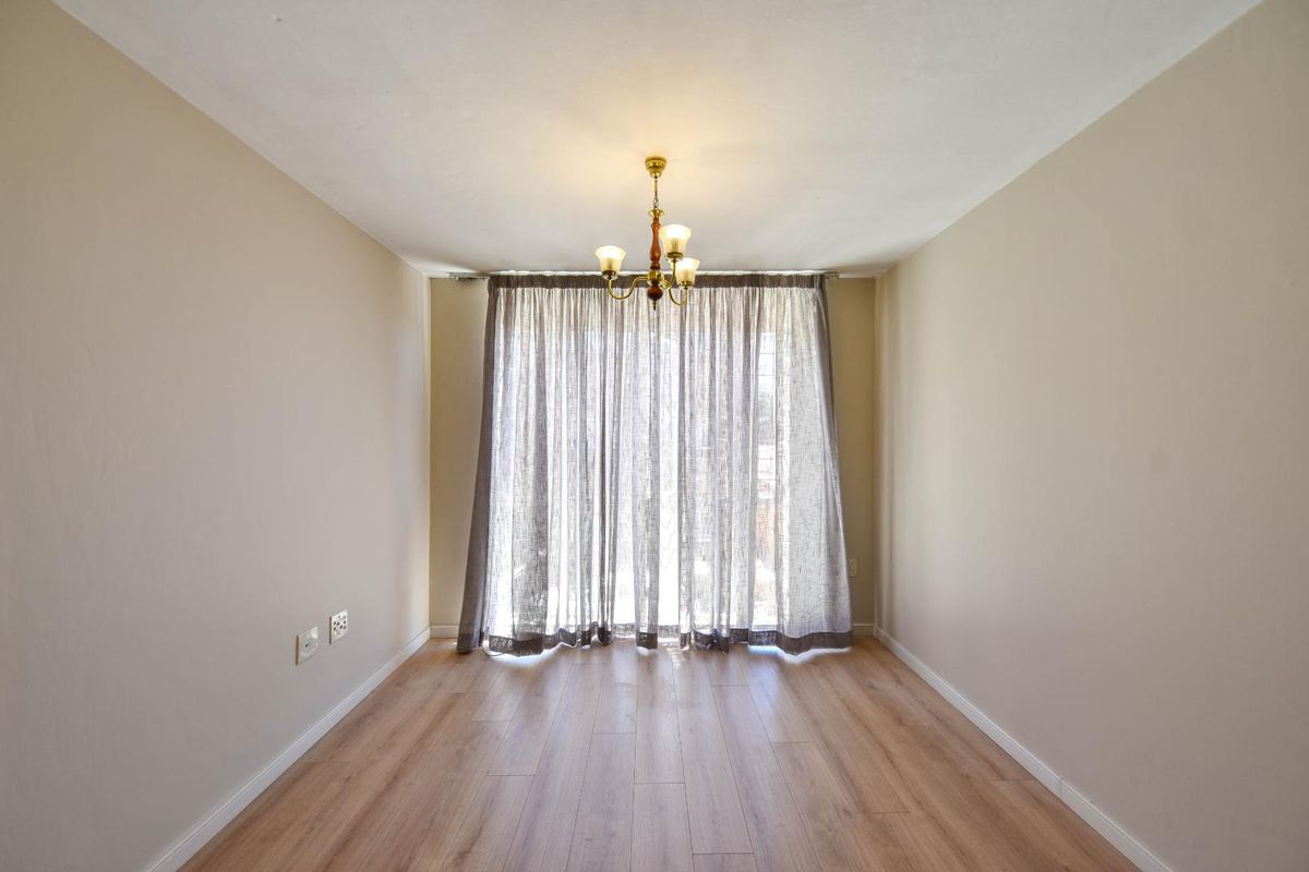 A bright and empty living room featuring light wood-look laminate flooring, neutral walls, and a sliding glass door with curtains leading to the exterior.