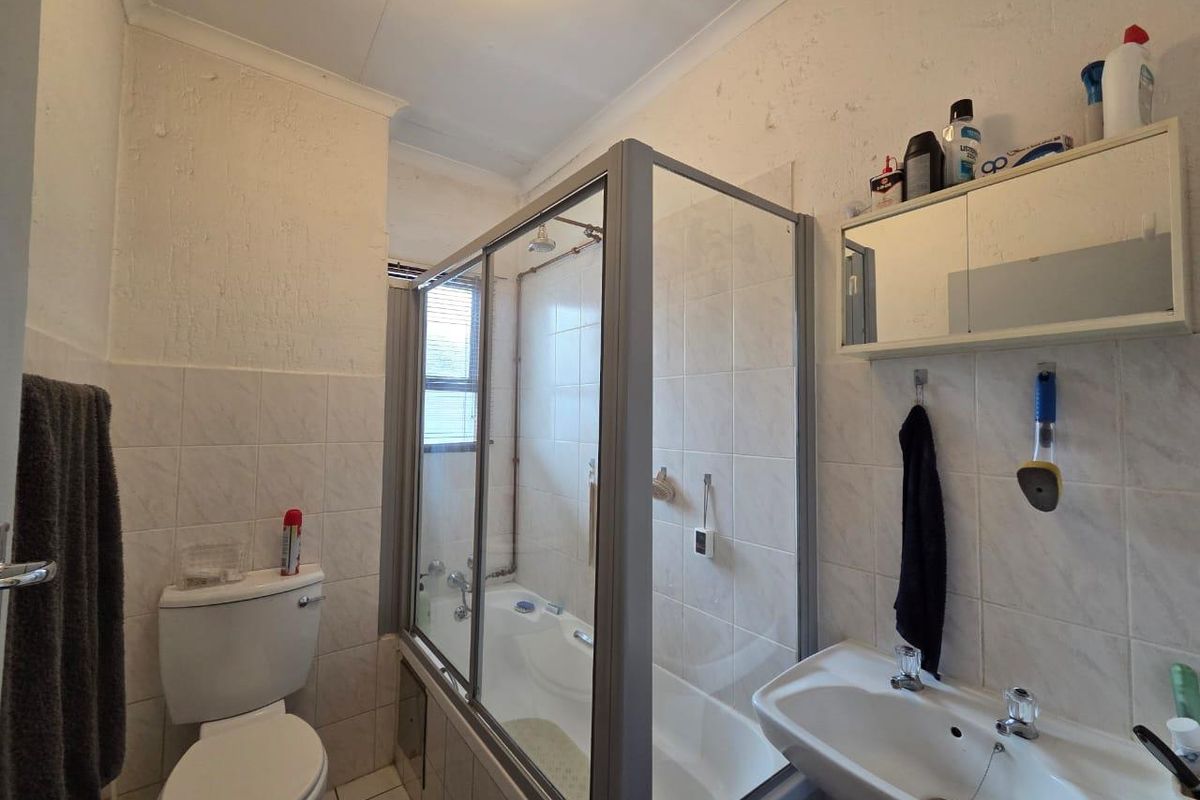 A functional bathroom featuring a shower-over-bath combination, a standard toilet, and a wall-mounted basin with a mirrored medicine cabinet.