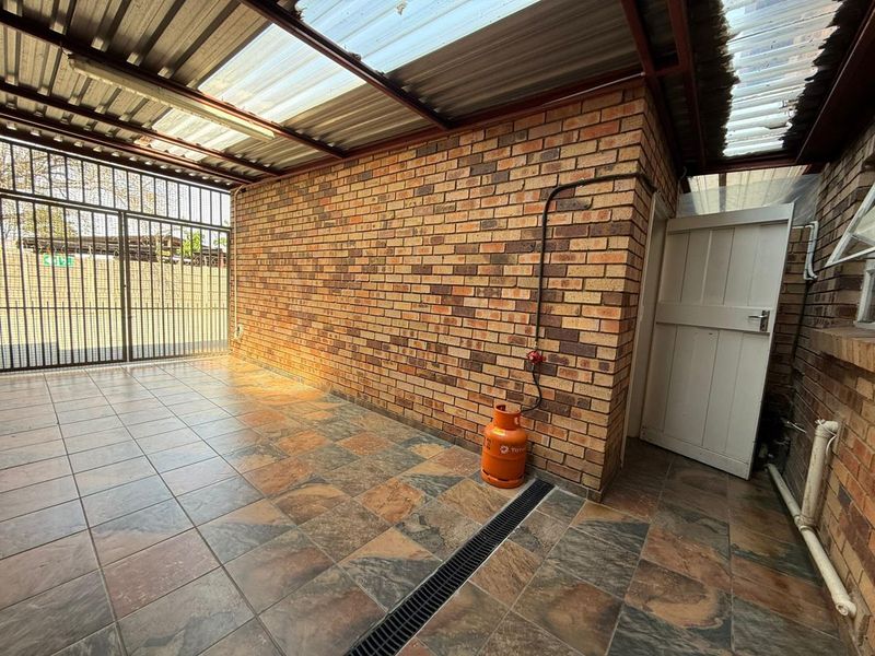 A covered outdoor patio area featuring tiled flooring, a brick wall, and a corrugated roof, providing a functional space for outdoor living.