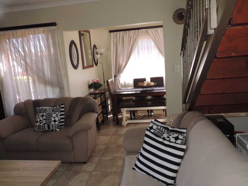 Open plan living and dining area featuring tiled flooring and a wooden staircase with a metal balustrade.