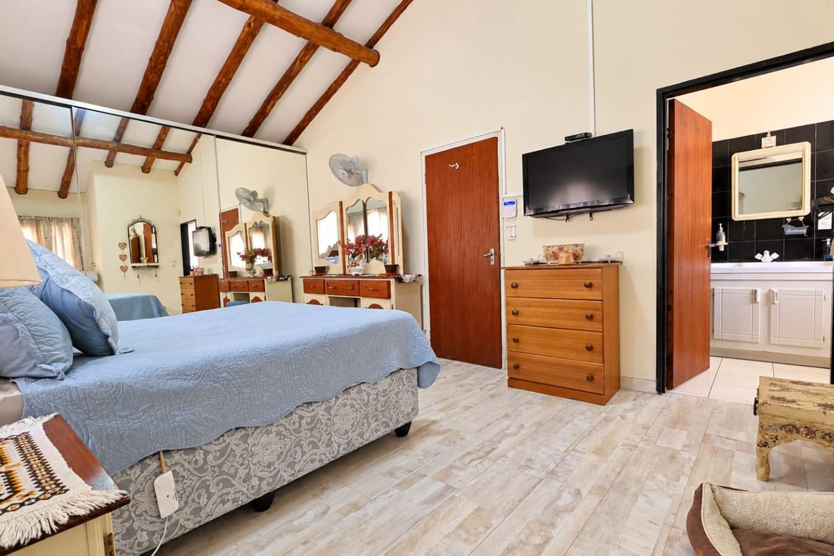 Spacious bedroom featuring exposed timber ceiling beams, tiled flooring, and a mirrored built-in wardrobe, with direct access to an en-suite bathroom.