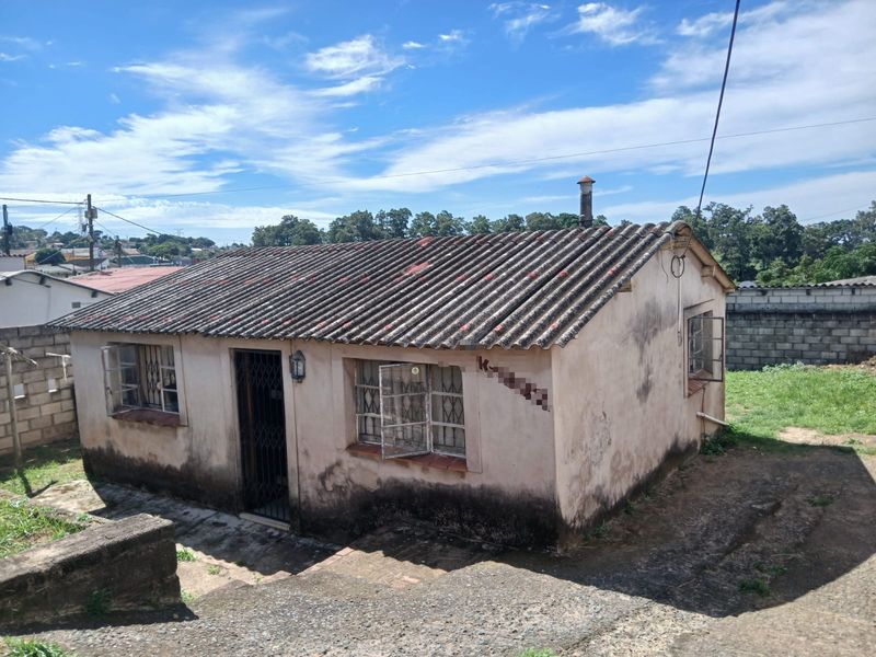 A detached residential structure featuring a corrugated roof and steel window frames, showing significant signs of exterior wear and maintenance requirements.