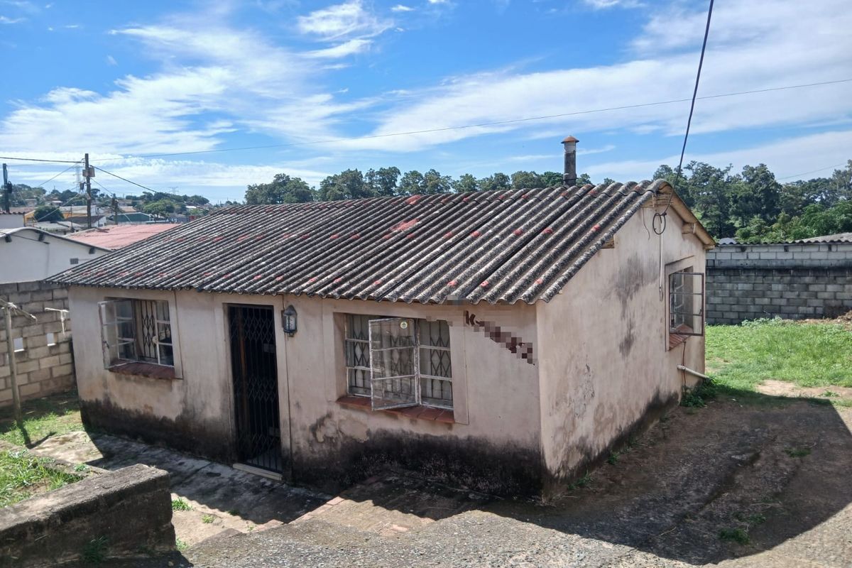 A detached residential structure featuring a corrugated roof and steel window frames, showing significant signs of exterior wear and maintenance requirements.