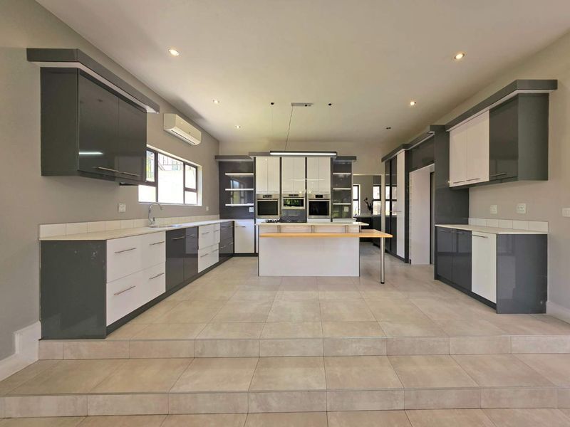 A spacious, modern kitchen featuring high-gloss cabinetry, a central island with integrated appliances, tiled flooring, and recessed lighting in an open-plan layout.