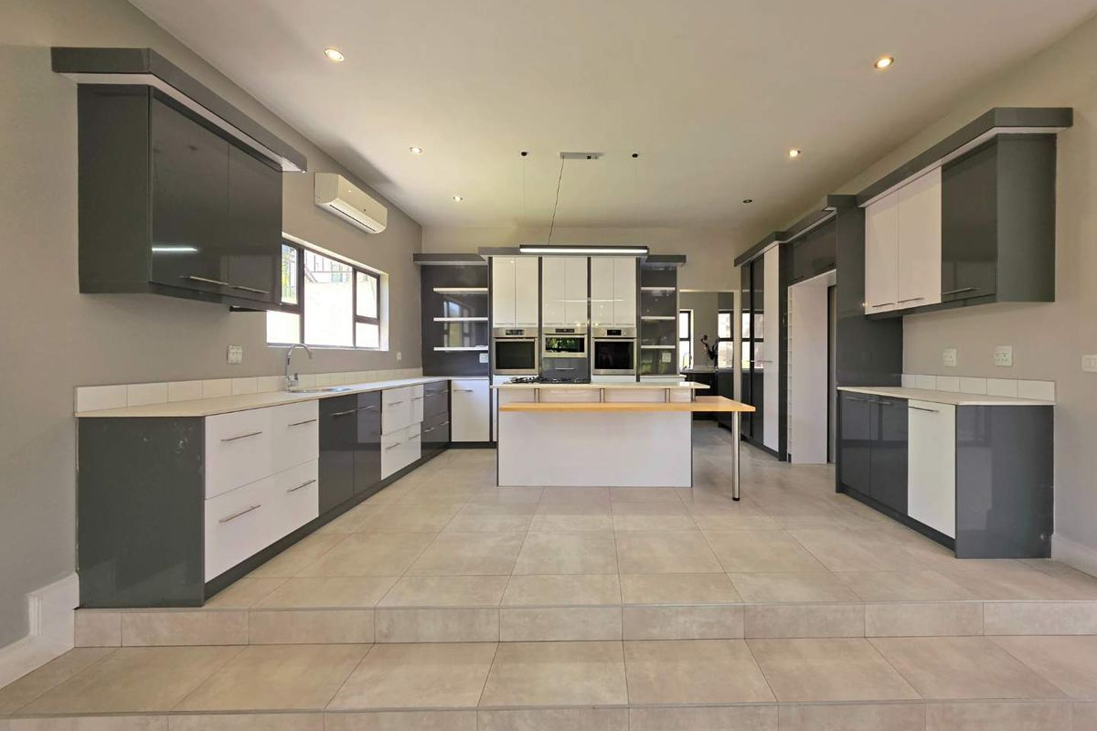 A spacious, modern kitchen featuring high-gloss cabinetry, a central island with integrated appliances, tiled flooring, and recessed lighting in an open-plan layout.