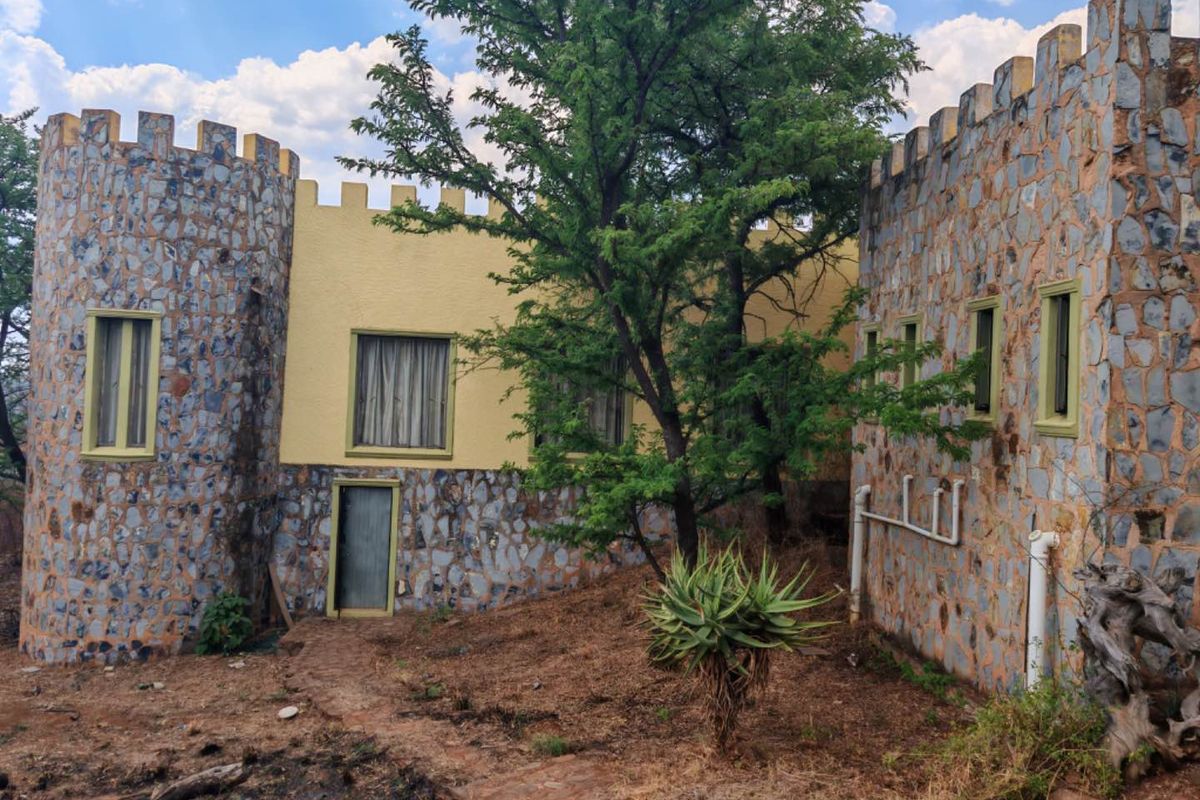 Rear exterior view of a unique castle-style building featuring stone masonry, crenellated parapets, and a natural garden setting.