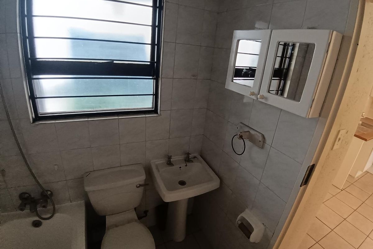 A functional bathroom featuring a pedestal basin, toilet, and bathtub with tiled walls and a window with security bars.